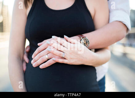 Mittelteil der Mann das Berühren der schwangeren Frau Bauch, während auf der Straße in der Stadt Stockfoto