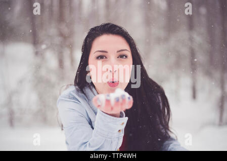 Portrait von teenage Mädchen bläst Schnee beim Stehen in Wald Stockfoto