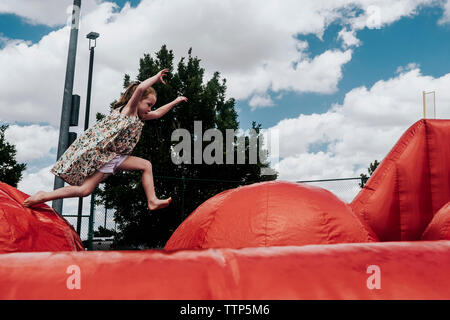 Seitenansicht der glücklichen Mädchen springen auf Hüpfburg gegen bewölkter Himmel im Park Stockfoto