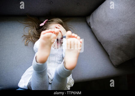 Hohe Betrachtungswinkel der glücklichen Mädchen verstecken Gesicht beim Liegen auf dem Sofa zu Hause Stockfoto