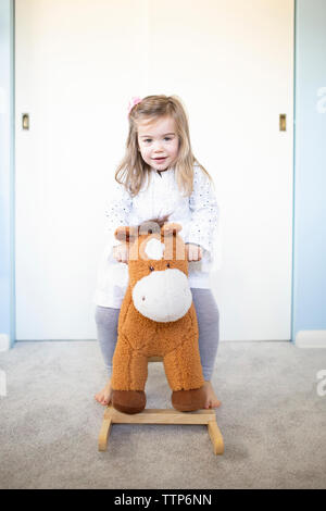 Portrait von cute girl auf Schaukelpferd gegen die Wand zu Hause sitzen Stockfoto