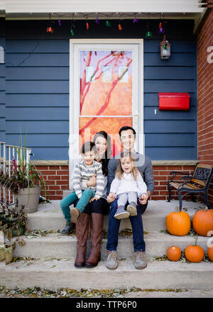 Portrait von lächelnden Familie sitzt auf Schritte gegen Haus während der Halloween Stockfoto