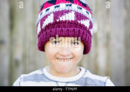 Close-up Portrait von Happy Boy Aufeinanderpressen der Zähne beim Stehen gegen Zaun im Hof Stockfoto