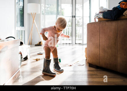 Kleinkind tragen Gummistiefel während Schnuller zu Hause saugen Stockfoto