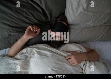 Hohe Betrachtungswinkel von Mann, Schlafmaske, während am Bett zu Hause schlafen Stockfoto