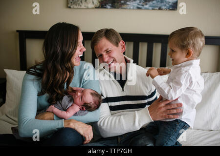Glückliche Eltern mit Kindern auf dem Bett zu Hause sitzen Stockfoto