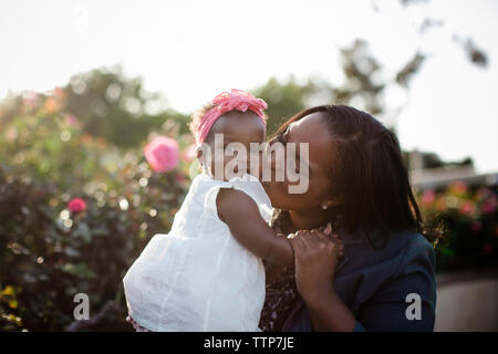 Glückliche Mutter küssen Tochter während der Sitzung von den Pflanzen im Park Stockfoto
