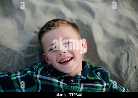 Hohen winkel Portrait von niedlichen Happy Boy liegen auf Sand am Strand bei Sonnenuntergang Stockfoto