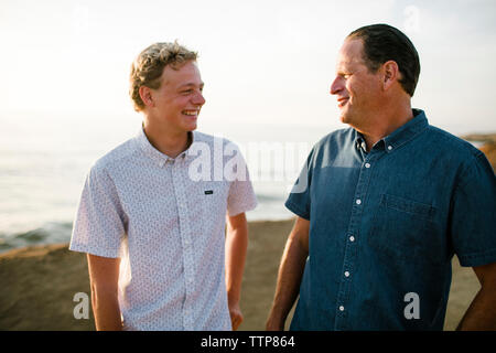 Gerne Vater mit Sohn beim Stehen auf Klippe gegen Meer bei Sonnenuntergang Stockfoto