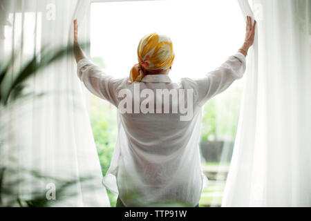 Ansicht der Rückseite des reife Frau Eröffnung Vorhänge am Fenster Stockfoto