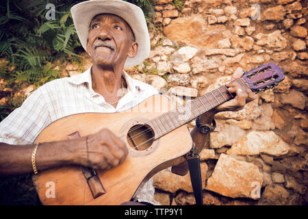 Man Gitarre spielen während der Sitzung gegen die Mauer aus Stein Stockfoto