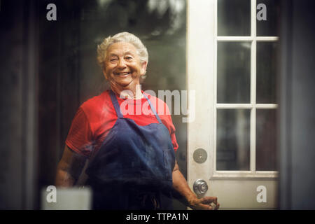 Portrait von lächelnden Eigentümer stehen vor der Tür der Küche durch das Fenster Glas gesehen Stockfoto