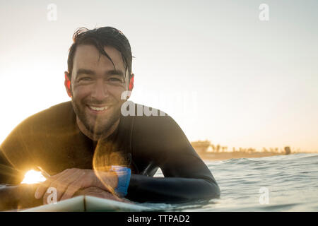 Portrait von Happy männliche Surfer liegen auf Surfbrett im Meer bei Sonnenuntergang Stockfoto