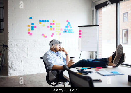 Nachdenklich Geschäftsmann holding Einweg Becher und kreative Büro zu sitzen Stockfoto