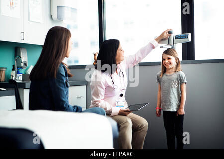 Die Ärztin messen Mädchen Höhe, während Mutter sitzt an der Klinik Stockfoto