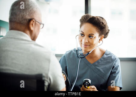 Lächelnd weibliche Arzt Kontrolle Blutdruck der männlichen Patienten in der Klinik Stockfoto