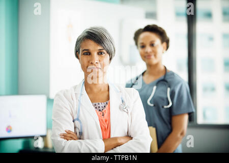 Portrait von zuversichtlich Ärztin stehende Arme mit Kollegen im Hintergrund gekreuzt Stockfoto