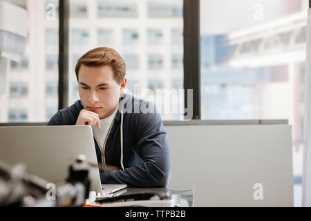 Männliche Kursteilnehmer mit Laptop am Tisch im Klassenzimmer konzentriert Stockfoto
