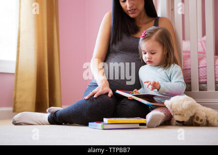 Nahaufnahme der schwangeren Frau mit Tochter im Buch suchen Stockfoto