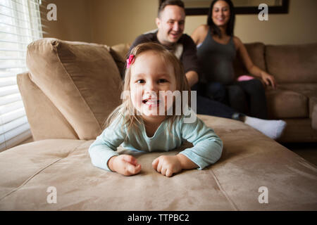 Portrait von niedlichen Mädchen liegt, während die Eltern auf dem Sofa zu Hause sitzen Stockfoto