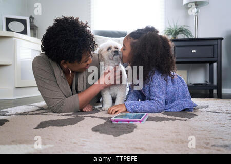 Glückliche Mutter an Tochter küssen Lhasa Apso während auf Teppich zu Hause liegen Stockfoto