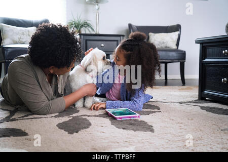 Mutter und Tochter spielen mit Lhasa Apso beim Lügen auf Teppich zu Hause Stockfoto