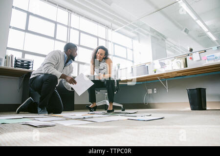 Low Angle View von Mitarbeitern der Organisation von Dokumenten auf Fußboden im Büro Stockfoto