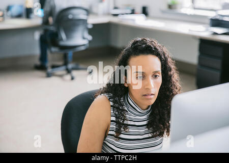 Geschäftsfrau, die Computer benutzt, während männlicher Kollege im Hintergrund ist Stockfoto