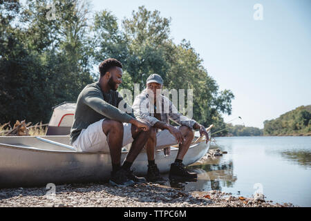 Männliche Freunde sprechen während der Sitzung auf dem Boot am Seeufer gegen den klaren Himmel Stockfoto