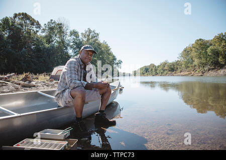 Porträt der Mann mit Angelrute beim Sitzen auf dem Boot am Seeufer Stockfoto