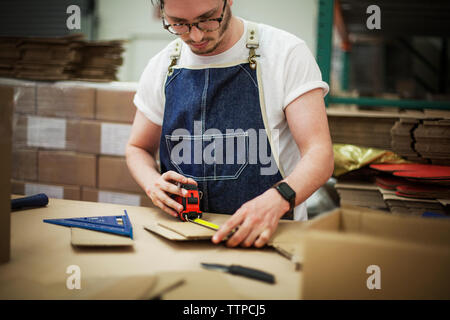 Mittelteil der männlichen Arbeitnehmer messen Karton im Lager Stockfoto