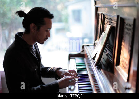 Man Klavier spielen gegen Fenster zu Hause Stockfoto