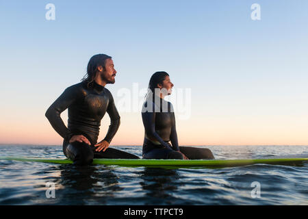 Nachdenkliche junge Paar entspannend auf Surfboards im Meer bei Sonnenuntergang Stockfoto