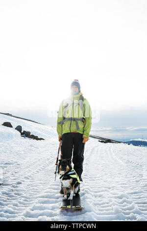 Mann mit Hund auf schneebedeckten Feld während Wandern Stockfoto