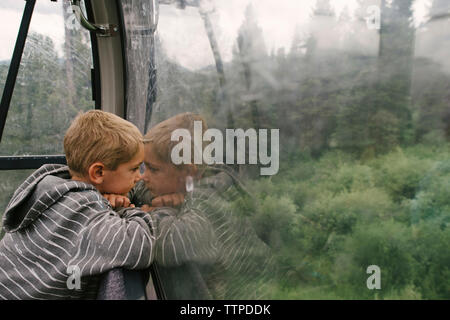 Seitenansicht des Jungen auf der Suche durch das Fenster während der Fahrt in der Seilbahn Stockfoto