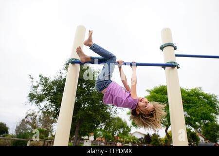 Verspielte Mädchen kopfüber an der Monkey Bars am Spielplatz gegen den klaren Himmel Stockfoto