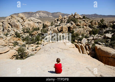 Ansicht der Rückseite des jungen Blick auf Felsformationen beim Sitzen im Joshua Tree National Park gegen Sky Stockfoto