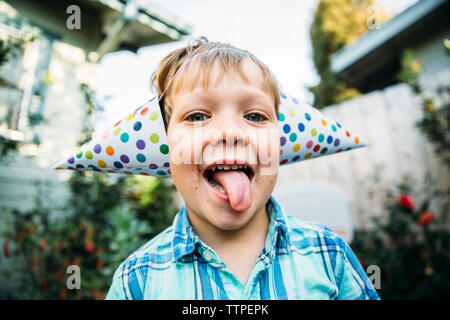 Portrait von glücklichen jungen in parteihüte heraus haften Zunge, während im Hinterhof stand Stockfoto