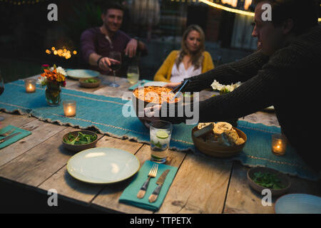 Mann, der Schüssel auf dem Tisch, während beim Abendessen mit Freunden im Patio Stockfoto