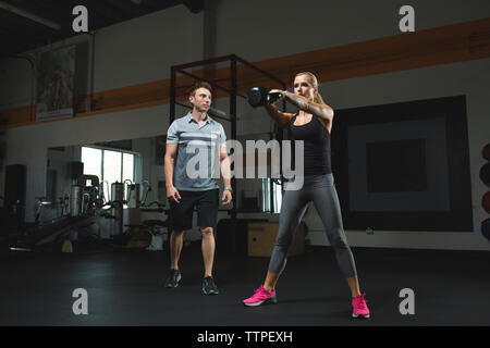Trainer suchen bei Frau heben kettlebell während des Trainings in der Turnhalle Stockfoto