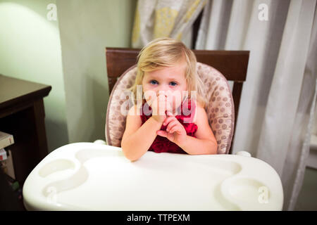 Portrait von niedlichen Baby Mädchen Saugen Daumen beim Sitzen auf hohen Stuhl zu Hause Stockfoto