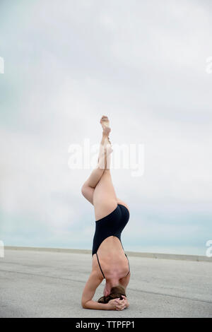 Ansicht der Rückseite des flexiblen Frau einen Badeanzug tragen beim Üben Kopfstand auf der Straße gegen den Himmel Stockfoto