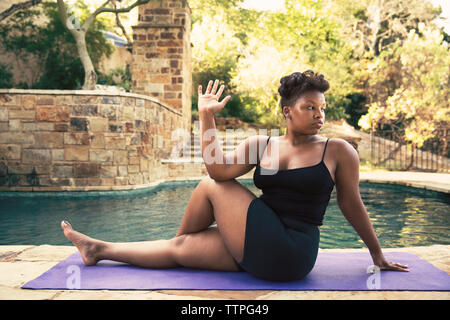 Selbstbewusste Frau, spinale Torsion auf Matte am Pool Stockfoto