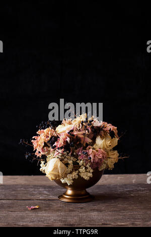 Nahaufnahme der Blumenvase auf Holztisch auf schwarzem Hintergrund Stockfoto