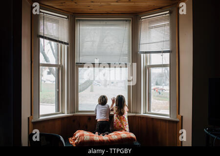 Ansicht der Rückseite des Geschwister durch Fenster zu Hause kniend Stockfoto