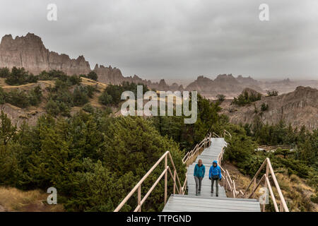 Mutter und Tochter klettern auf hölzernen Stufen beim Wandern inmitten von Bergen in Badlands National Park Stockfoto