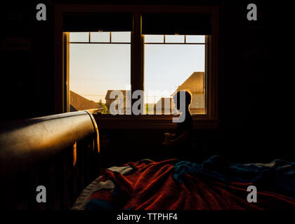 Junge durch Fenster in dunklen Zimmer Stockfoto