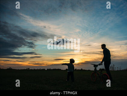 Silhouette von Vater und Sohn zu Fuß mit dem Fahrrad auf dem Feld bei Sonnenuntergang Stockfoto