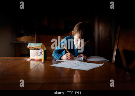 Ein junger kleiner Junge Hausaufgaben an einem Tisch Stockfoto