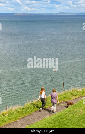 TENBY, Pembrokeshire, Wales - AUGUST 2018: Leute, die einen Hund auf dem Wanderweg rund um den Schlossberg in Tenby, West Wales. Stockfoto